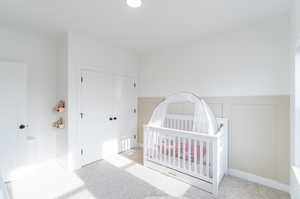 Bedroom with light carpet, a nursery area, and a closet