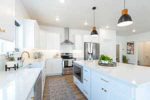 Kitchen featuring wall chimney range hood, hanging light fixtures, white cabinets, and appliances with stainless steel finishes