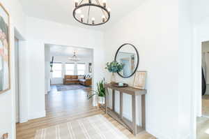 Hallway with light LVP floors and a notable chandelier