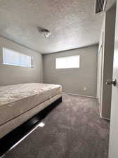 Bedroom with dark colored carpet and a textured ceiling