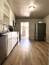 Kitchen featuring a textured ceiling, appliances with stainless steel finishes, white cabinets, hardwood / wood-style floors, and sink