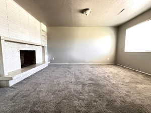 Room with a textured ceiling, carpet flooring, and a large fireplace