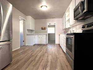 Kitchen with light hardwood / wood-style flooring, a textured ceiling, backsplash, white cabinets, and appliances with stainless steel finishes