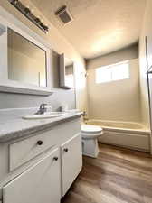 Full bathroom featuring a textured ceiling, washtub / shower combination, wood-type flooring, vanity, and toilet