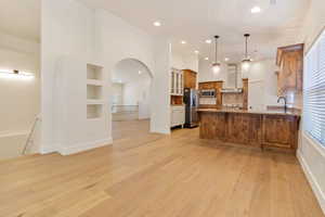 Kitchen featuring wall chimney exhaust hood, light hardwood / wood-style floors, stainless steel appliances, and decorative light fixtures