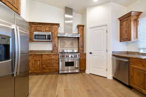 Kitchen featuring tasteful backsplash, stainless steel appliances, light wood flooring, granite counter tops, and wall chimney range hood