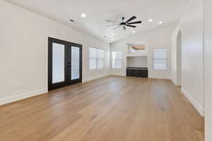 Great room with ceiling fan, lofted ceiling, light hardwood floors, and french doors