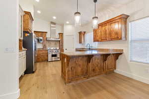 Kitchen with wall chimney range hood, light wood-type flooring, stainless steel appliances, kitchen peninsula, and pendant lighting