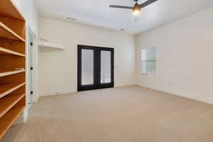 Primary bedroom with light colored carpet, ceiling fan, and french doors