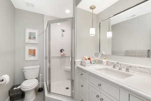 Bathroom featuring a shower with door, toilet, and vanity