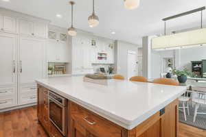 Kitchen with a center island, white cabinetry, light wood-type flooring, pendant lighting, and tasteful backsplash