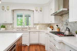 Kitchen featuring stainless steel gas cooktop, hardwood / wood-style floors, white cabinetry, wall chimney exhaust hood, and sink