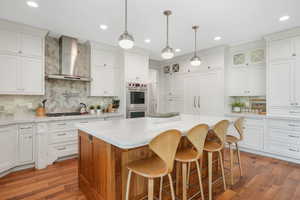 Kitchen featuring wall chimney range hood, a kitchen island, stainless steel appliances, hardwood / wood-style flooring, and tasteful backsplash