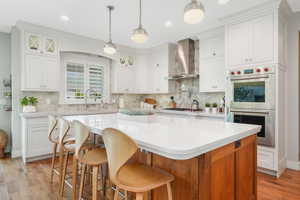 Kitchen featuring light hardwood / wood-style flooring, backsplash, wall chimney range hood, white cabinetry, and appliances with stainless steel finishes