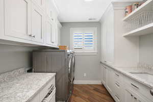 Clothes washing area featuring cabinets, dark wood-type flooring, and washer and clothes dryer