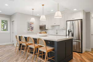 Kitchen with light hardwood / wood-style flooring, stainless steel appliances, white cabinets, kitchen peninsula, and backsplash