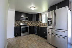 Kitchen featuring appliances with stainless steel finishes, sink, backsplash, and light stone counters