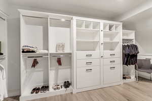 Walk in closet with light hardwood / wood-style flooring