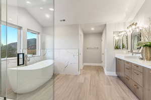 Bathroom featuring vaulted ceiling, tile walls, hardwood / wood-style flooring, a tub, and vanity