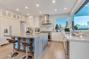 Kitchen with stainless steel range, light wood-type flooring, light stone counters, wall chimney range hood, and white cabinetry