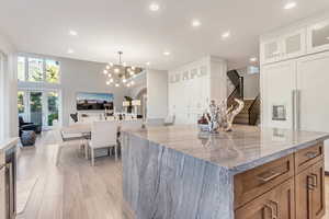 Kitchen featuring light hardwood / wood-style flooring, light stone counters, a center island, white cabinetry, and a chandelier