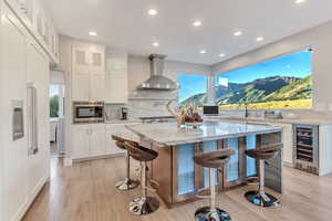 Kitchen with wine cooler, a mountain view, built in appliances, light wood-type flooring, and wall chimney range hood