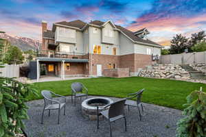 Back house at dusk featuring a patio area, a fire pit, a mountain view, and a lawn