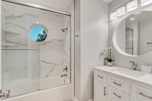 Bathroom with vanity and bath / shower combo with glass door