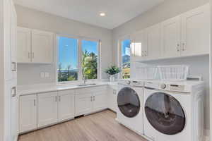 Laundry room with sink, light hardwood / wood-style flooring, cabinets, and washing machine and clothes dryer