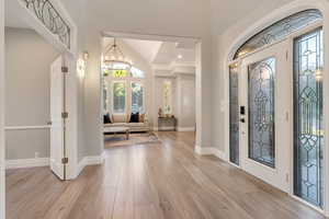 Foyer with an inviting chandelier, ornamental molding, light hardwood / wood-style flooring, and lofted ceiling