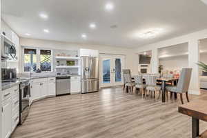 Kitchen with stainless steel appliances, white cabinetry, light hardwood / wood-style floors, and french doors