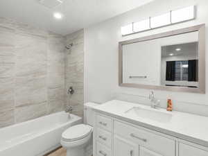 Full bathroom with a textured ceiling, vanity, toilet, and tiled shower / bath combo