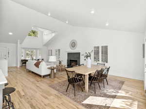 Dining space with high vaulted ceiling, light hardwood  floors, and a fireplace