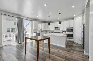 Kitchen with decorative light fixtures, dark hardwood / wood-style flooring, a kitchen island, backsplash, and appliances with stainless steel finishes