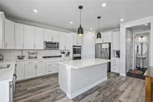 Kitchen featuring stainless steel appliances, tasteful backsplash, a center island, wood-type flooring, and white cabinets