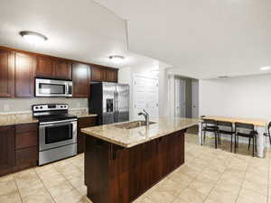 Kitchen featuring appliances with stainless steel finishes, sink, an island with sink, and light tile floors