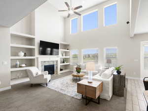 Living room with a premium fireplace, a towering ceiling, ceiling fan, and built in shelves