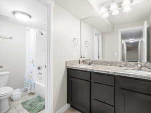 Full bathroom with tile floors, double vanity, toilet, and shower / bath combo with shower curtain