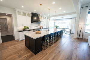 Kitchen featuring hanging light fixtures, premium range hood, a large island with sink, and wood-type flooring