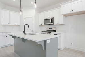 Kitchen with white cabinets, decorative light fixtures, stainless steel appliances, and an island with sink