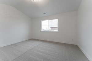 Carpeted empty room featuring lofted ceiling