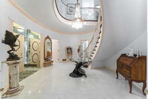 Tiled foyer entrance with a notable chandelier, a towering ceiling, and crown molding