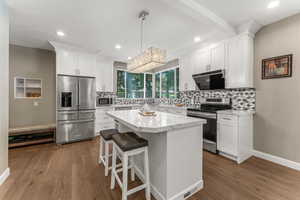 Kitchen featuring a center island, appliances with stainless steel finishes, backsplash, engineered  flooring, and pendant lighting.