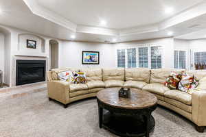 Living room featuring a raised ceiling, a tiled fireplace, carpet flooring, and ornamental molding