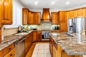 Kitchen featuring stainless steel appliances, light stone counters, sink, tasteful backsplash, and custom exhaust hood