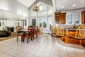 Tiled dining room featuring beamed ceiling, a tile fireplace, a notable chandelier, sink, and high vaulted ceiling