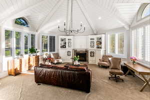 Carpeted living room with plenty of natural light, high vaulted ceiling, beamed ceiling, and a notable chandelier