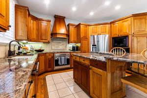 Kitchen with a kitchen breakfast bar, black appliances, premium range hood, light stone counters, and sink