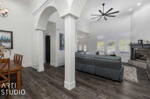 Living room featuring crown molding, dark wood-type flooring, a high end fireplace, ceiling fan with notable chandelier, and a high ceiling