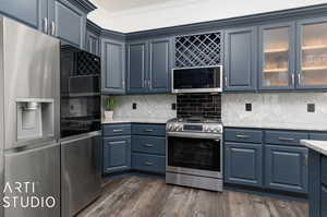 Kitchen featuring dark hardwood / wood-style flooring, backsplash, blue cabinets, ornamental molding, and appliances with stainless steel finishes